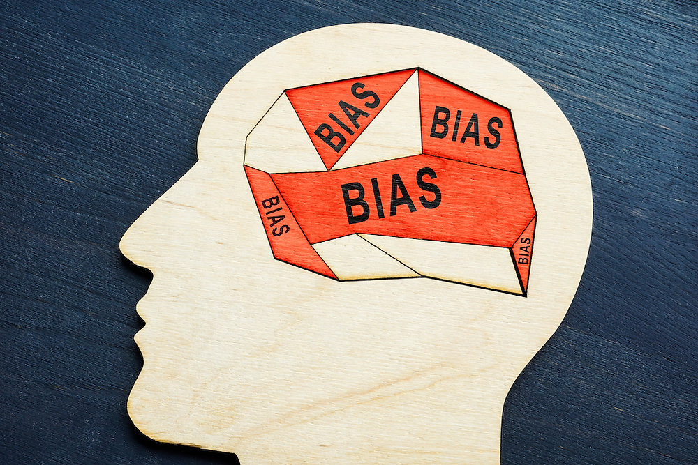 A wooden cutout of a human head with the word "BIAS" repeated inside a geometric brain-like structure. This image represents cognitive biases, which marketers leverage to influence consumer behavior and boost customer retention by aligning their strategies with how people make decisions.| www.genbmarketing.com